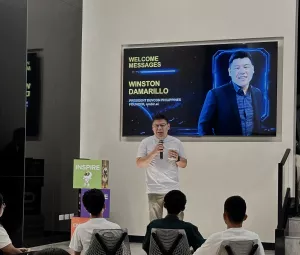 Winston Damarillo, President of DevCon Philippines and founder of nmbr.ai, delivers a welcome message to attendees at an AI and developer community event, speaking on stage with a presentation screen displaying his name and role in the background.
